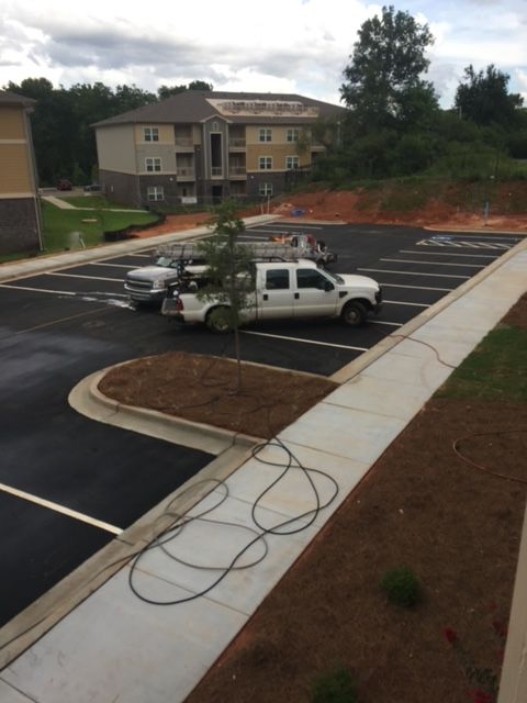 Parking lot with a white work truck parked near a building under construction. A concrete sidewalk runs along the right side of the frame.