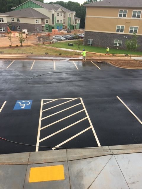 Asphalt parking lot with painted handicap symbol and access space. Two construction workers in neon vests are visible near buildings in the background.
