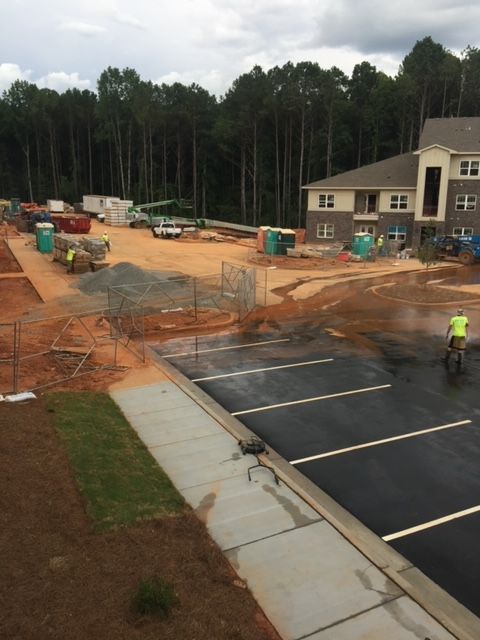 Construction site with new asphalt parking lot, partially built apartment buildings, and a rider on a motorcycle.