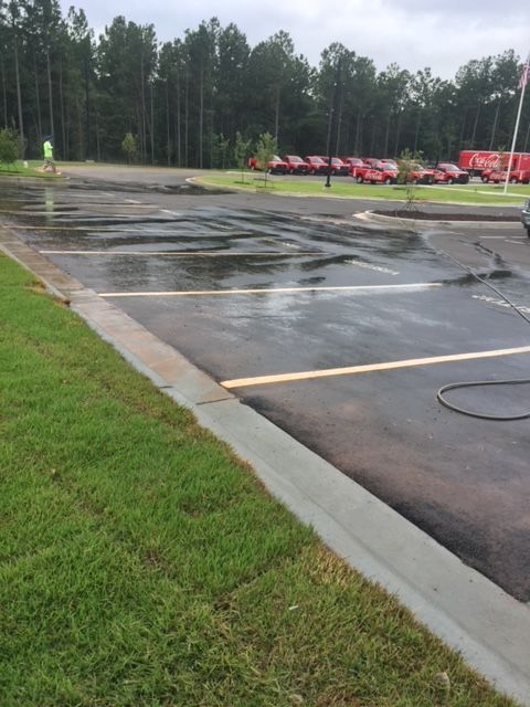 Wet parking lot with marked parking spaces and grassy edge. A person in a reflective vest is visible in the distance.