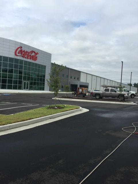 Coca-Cola facility with a red logo. A large building with a glass front and a parking lot in front.