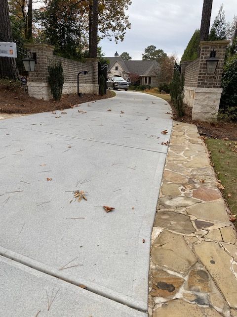 A concrete driveway leads to a house, flanked by brick pillars and a stone pathway. A car is parked near the home.
