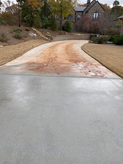 Concrete driveway leading to a stone house with a winding dirt patch.