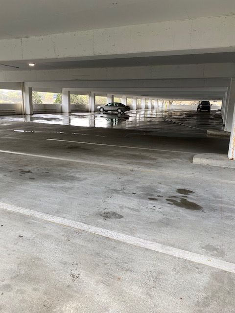 Empty, wet parking garage with a car parked in the distance. White concrete with puddles and visible support beams.