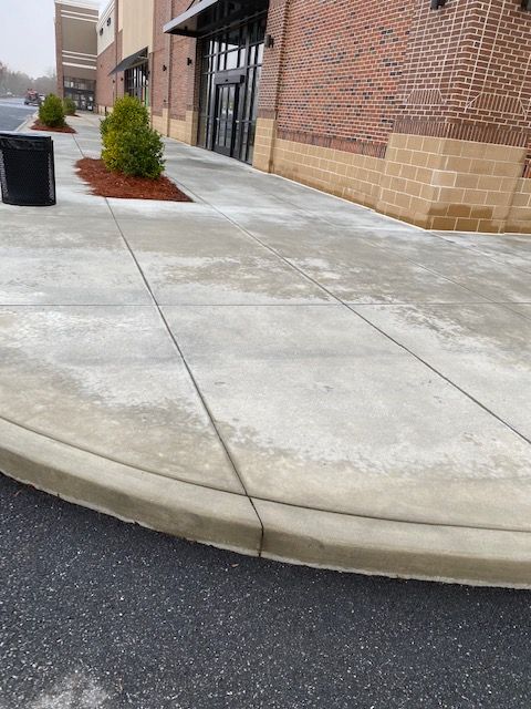 A concrete sidewalk curves toward an entrance with glass doors.  Brick and tan stone building exterior.