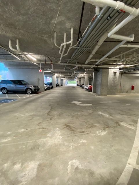 Parking garage interior with concrete columns, gray cars parked on either side, and a white arrow pointing forward.