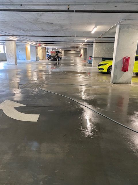 A freshly cleaned, shiny gray parking garage floor with a large white arrow. A yellow car is parked on the right.
