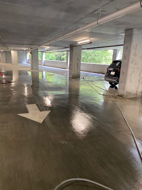 Wet concrete floor in a parking garage with a car in the background; a hose and a painted arrow are visible.
