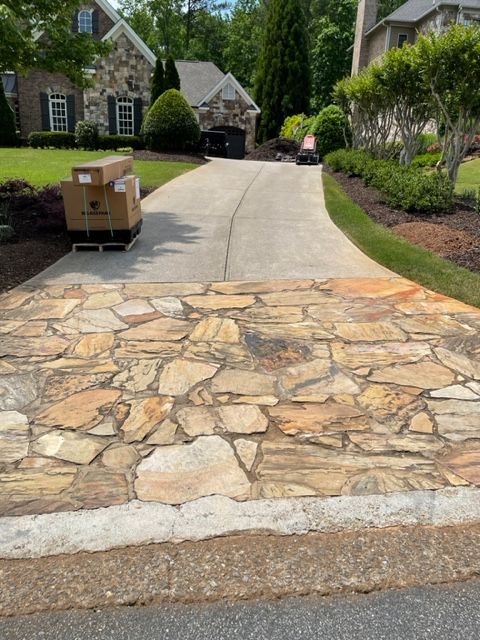 Stone-paved driveway leads to a house with a concrete driveway. A palette of boxes sits to the left.