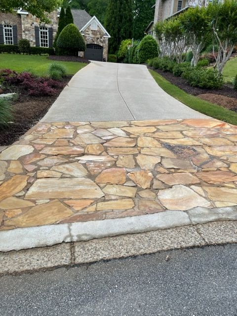 Driveway with a flagstone entrance, transitioning to concrete leading up to a house with landscaping.