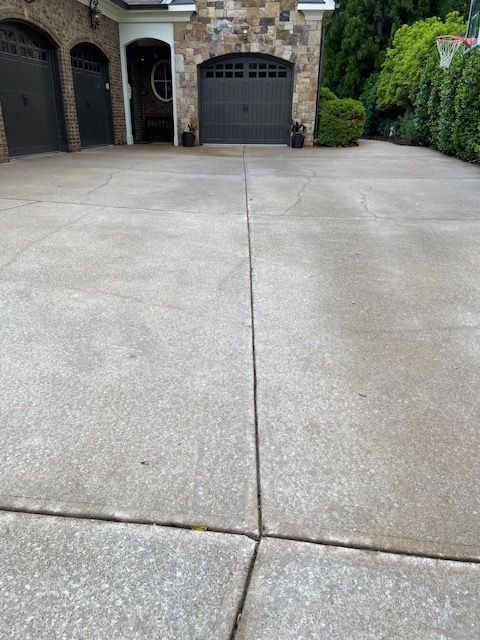 Concrete driveway leading to a two-car garage with a stone façade and dark gray doors. A vertical crack runs down the center of the driveway.