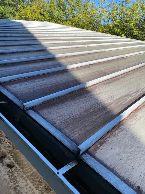Close-up view of a weathered metal roof with brown discoloration and a partially visible gutter.