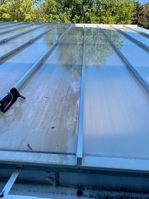A clear plastic roof being cleaned with a pressure washer. One side is dirty, the other side clean.