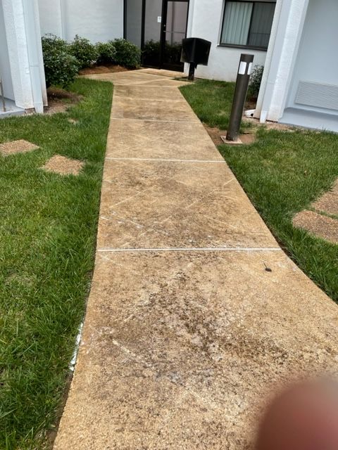 A concrete walkway leading towards a building, flanked by green grass. The walkway appears weathered.