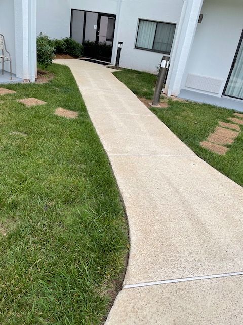 A paved walkway curves between green grass and white buildings.