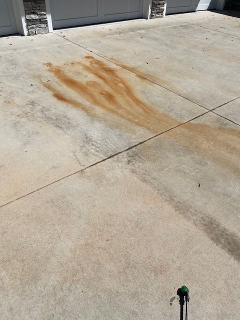 A concrete driveway stained with streaks of rust-colored liquid. The driveway is in front of a garage on a sunny day.