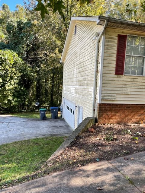 Side of a house with a white garage door, beige siding, and a red shutter. Driveway slopes down toward the side of the house.