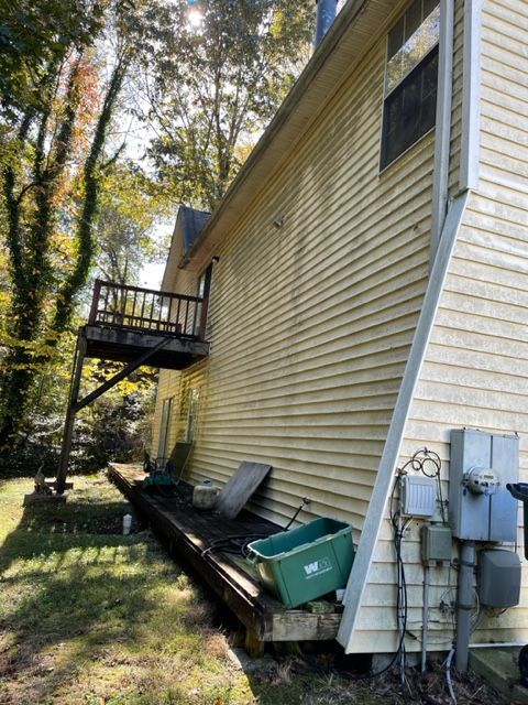 Yellow-sided house with a wooden deck. Green grass and trees surround the building with electrical boxes visible.