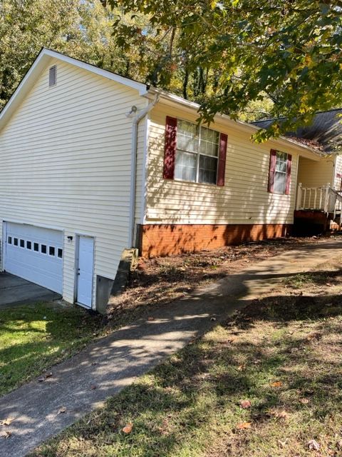 Beige house with a garage and red shutters on a sunny day. A driveway leads up to the house.