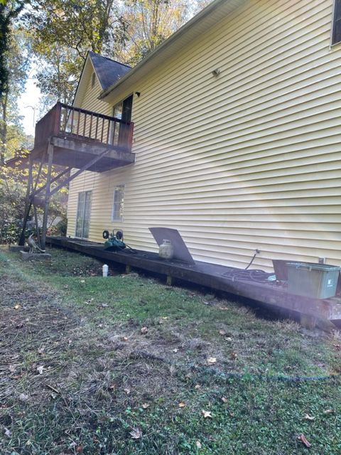A two-story yellow house with a wooden deck and a ground-level wooden platform. Green grass in front of the house.
