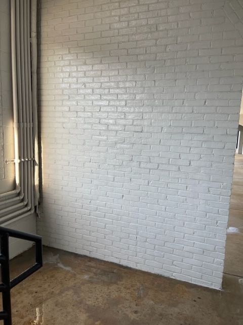 White-painted brick wall in an interior space, with pipes on the left and concrete floor in the foreground.