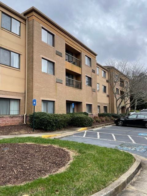 Three-story brick apartment building with accessible parking and a landscaped entrance on a cloudy day.