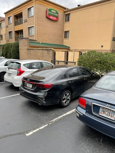 Black car parked in front of a hotel. Other cars are parked nearby on the asphalt. A Courtyard by Marriott sign is visible.