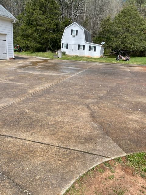 A concrete driveway with dark staining, a white barn-style building with black trim, and green grass.