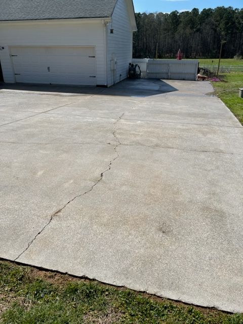 Cracked concrete driveway in front of a white garage and green lawn.