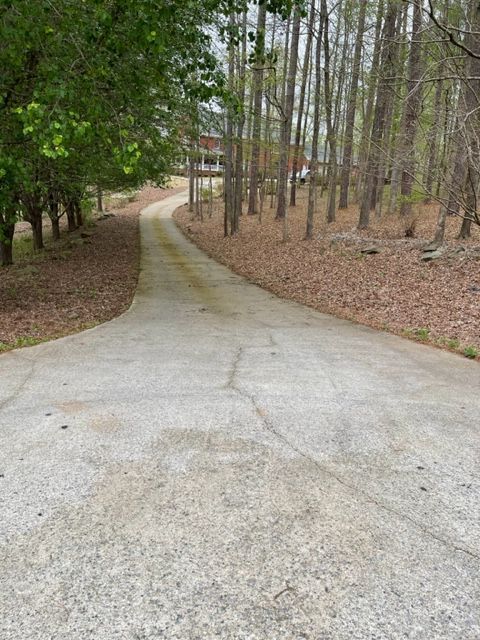 Concrete driveway winding uphill through a wooded area, leading to a distant house.