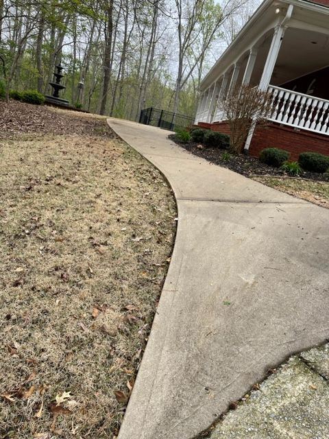 A concrete driveway curves towards a house with a white porch, and a fountain in the distance; the lawn is brown.