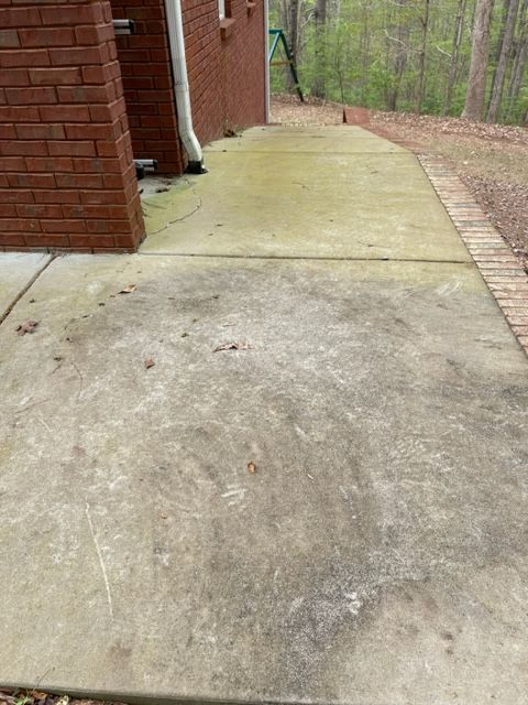 Concrete patio with brick trim and a brick wall. The concrete shows signs of weathering and discoloration.