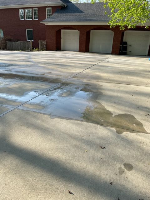 A wet concrete driveway in front of a brick house with three garage doors. Water puddles in the center.