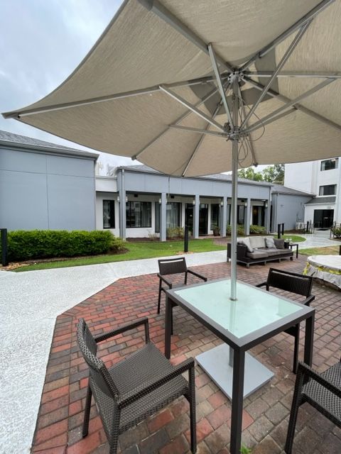 Patio seating with a table and chairs under a large umbrella, set on a brick and stone patio, with a building in the background.