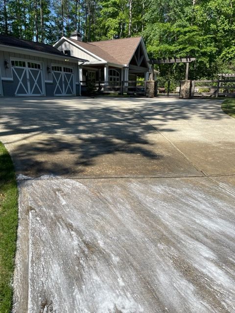 A concrete driveway with white streaks in front of a house and a wooden gazebo. Blue and white garage doors are visible on the left.