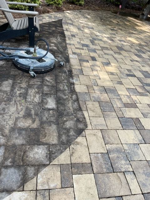 Pressure washer cleaning a brick patio; half is dirty, the other clean.