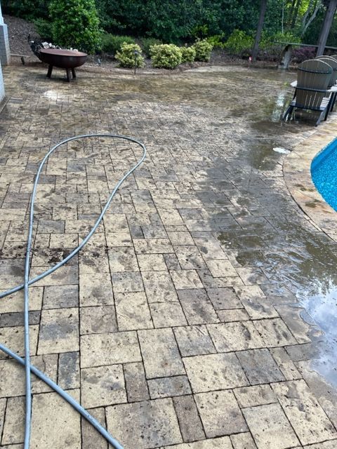 A brick patio partially wet from water, with a pool to the right. A hose and an outdoor fire pit are visible.