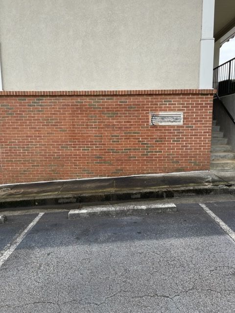 Brick wall with a small plaque, next to stairs and a parking space.