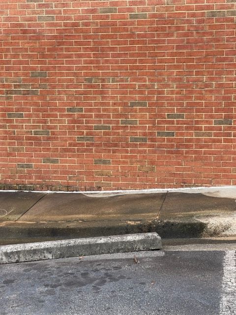 Red brick wall, weathered concrete curb, and dark asphalt pavement. The curb has a ramp.