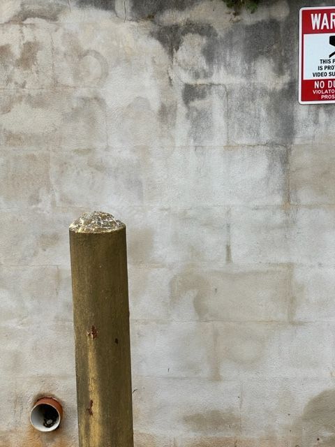 A weathered concrete wall with a wooden post in front. A warning sign is attached to the wall.