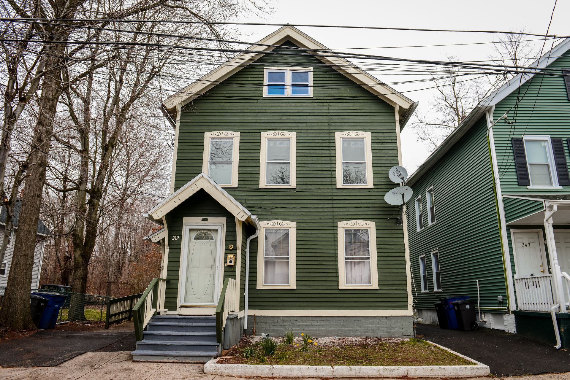 A two-story green house with a white-framed front door, light-colored window frames, and grey front steps.