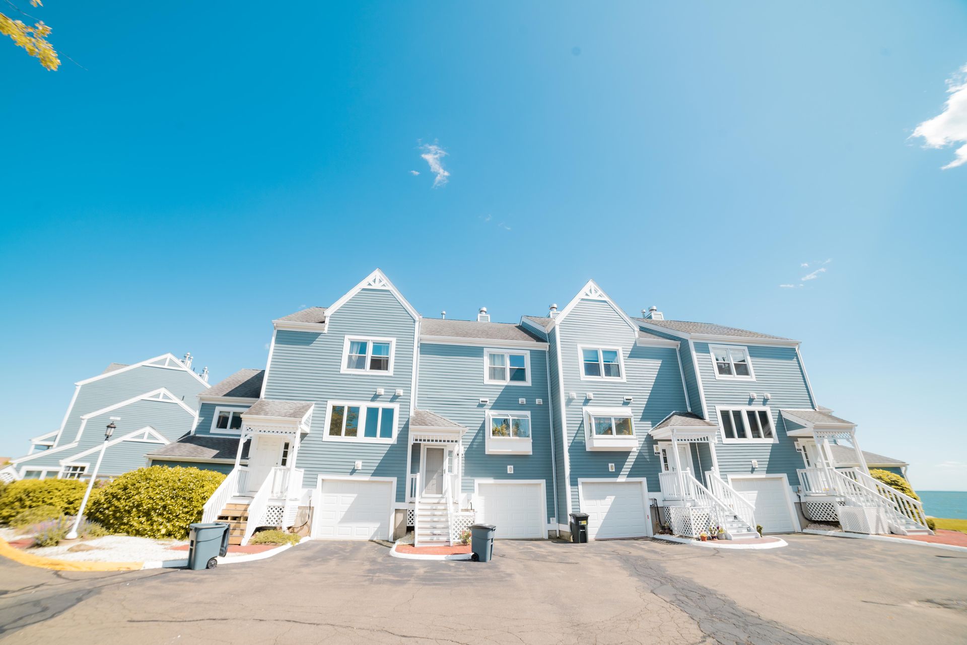 A multi-story blue townhouse complex with white trim and garage doors under a clear blue sky.