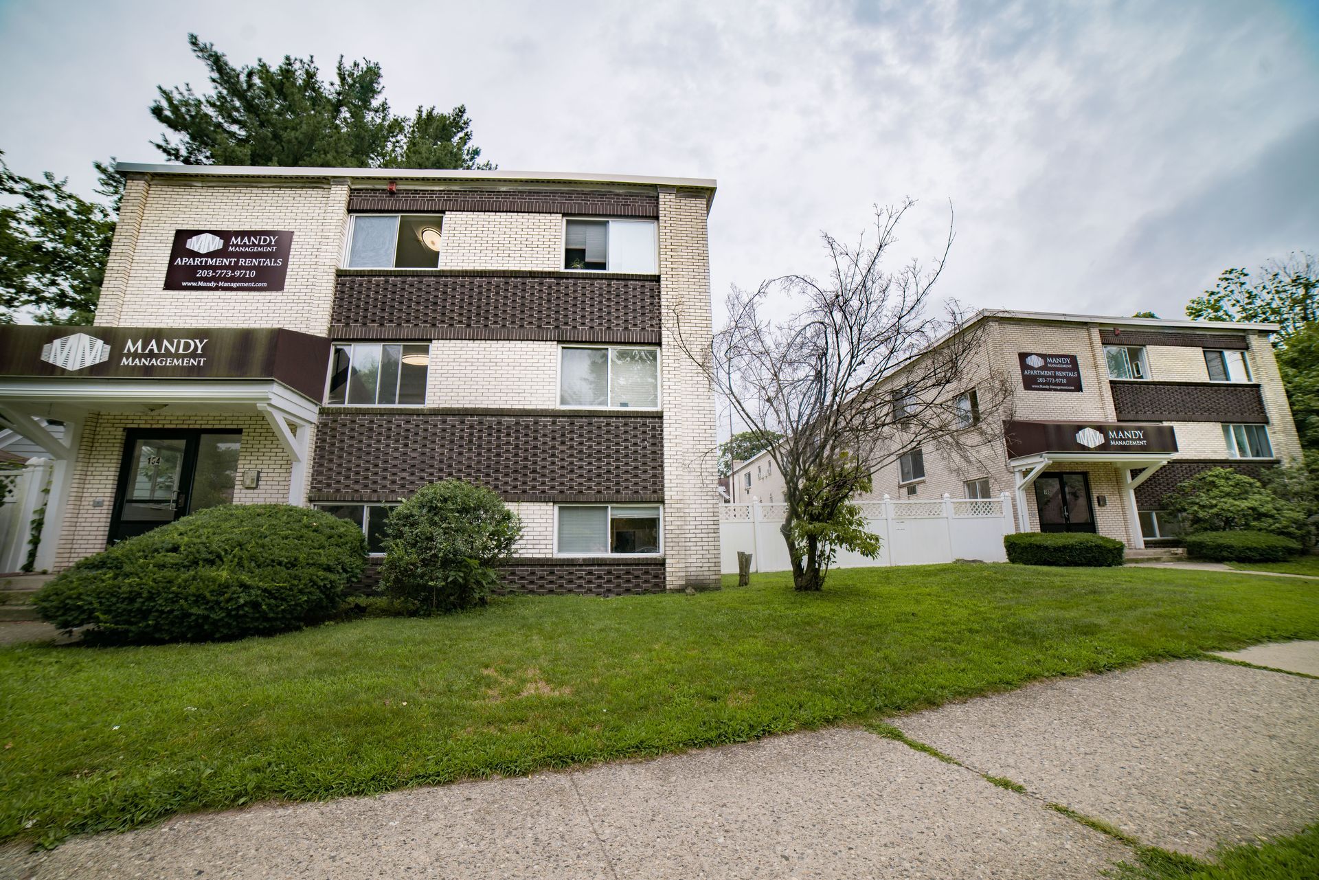 Two multistory apartment buildings with light stone and dark brown lattice-patterned walls under a cloudy sky.
