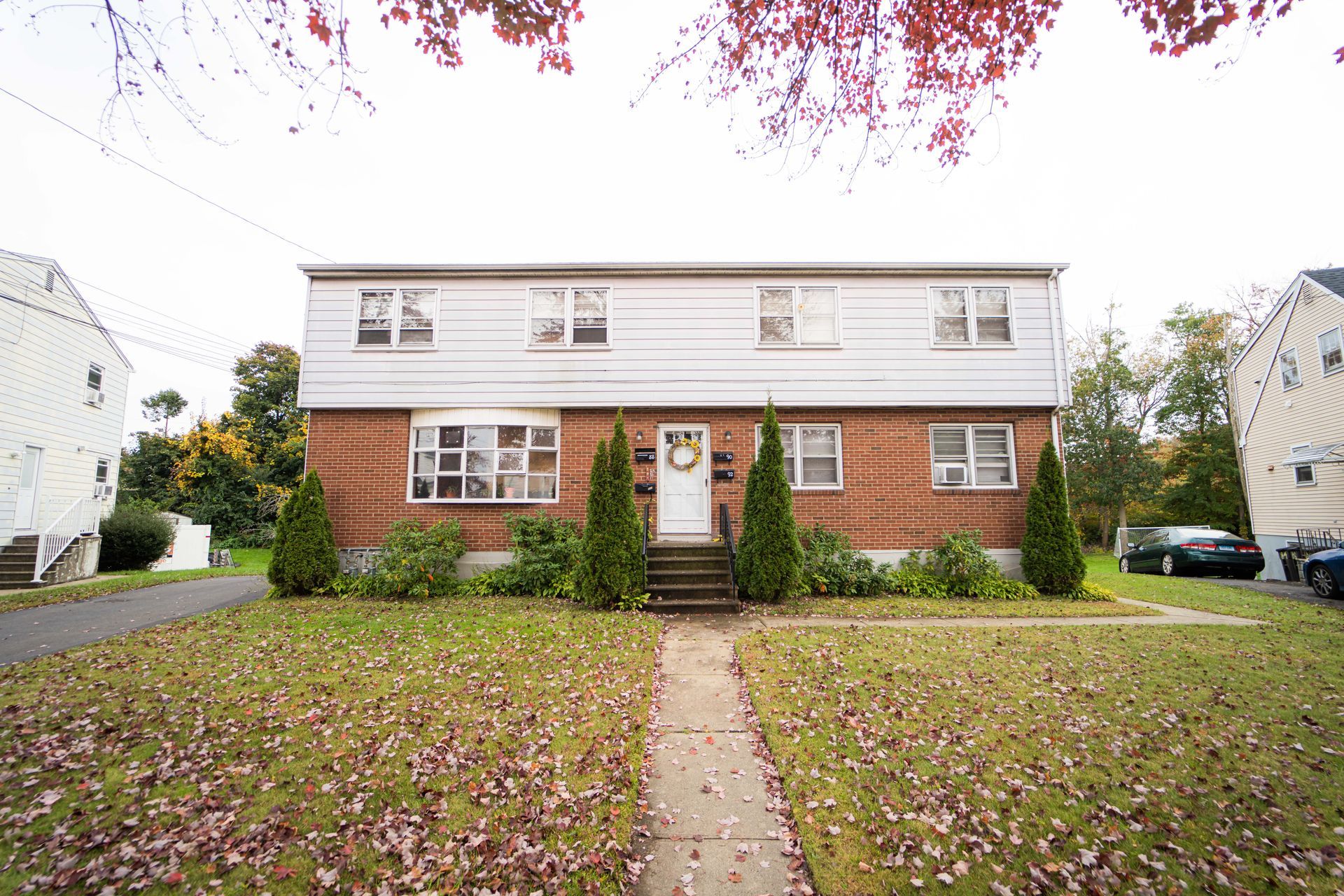 Two-story residential building with white siding on the upper half and brick on the lower half, with a front lawn.