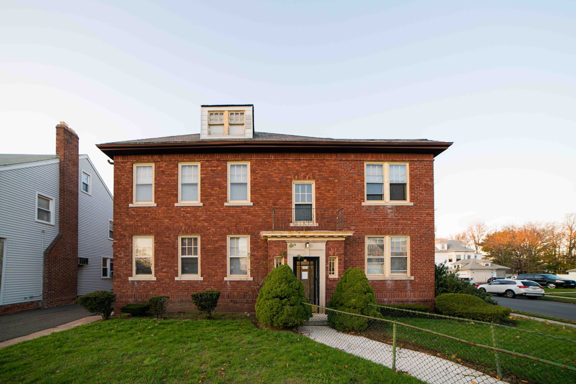 A two-story red brick apartment building with a central entrance, white trim, and a small dormer window on the roof.