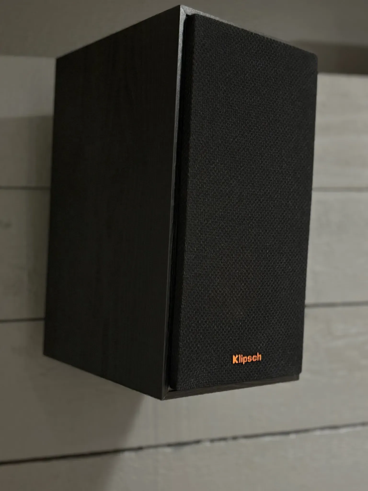 A black Klipsch bookshelf speaker mounted on a white paneled wall.
