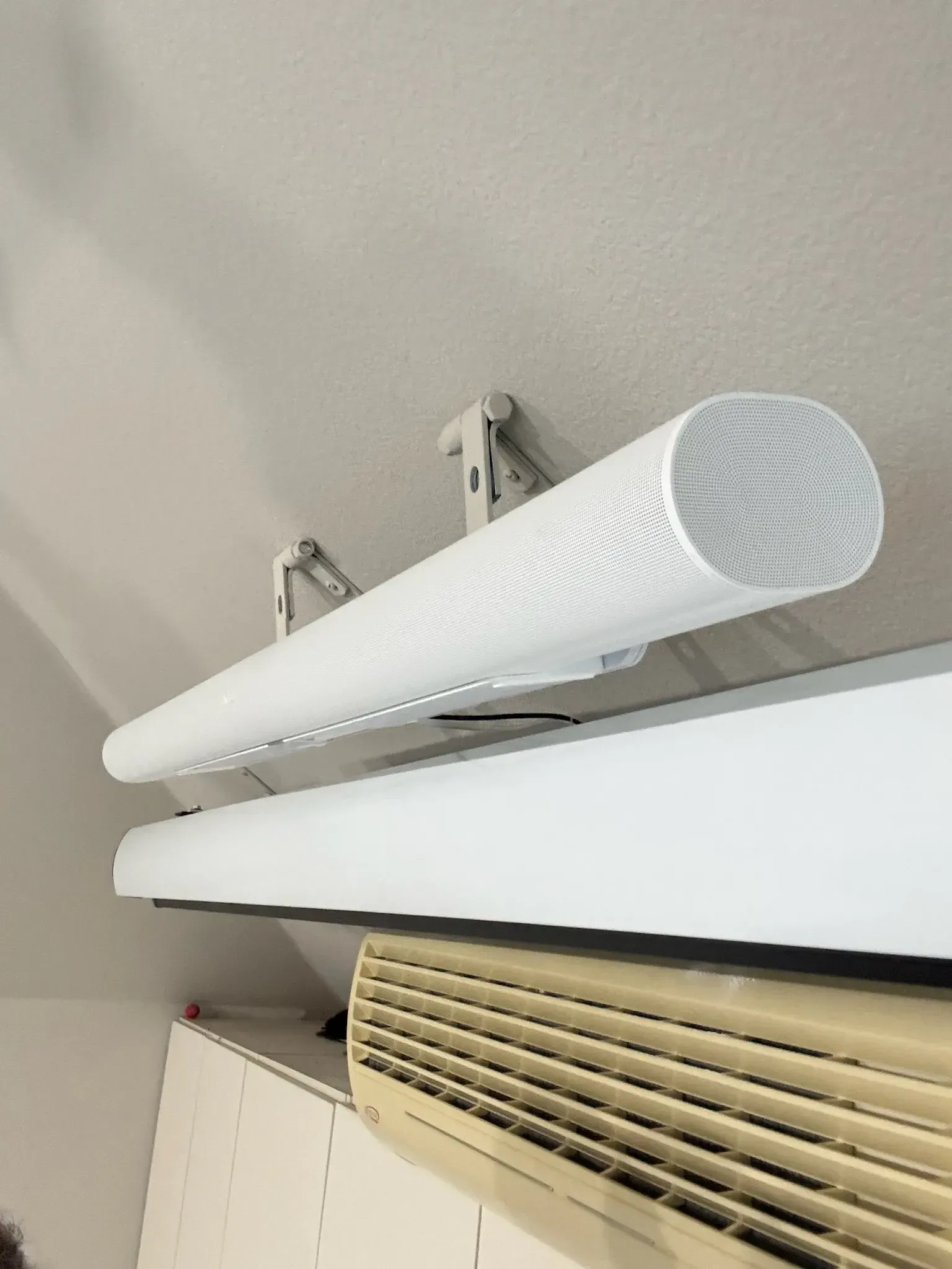 A white, cylindrical projection screen mounted to a ceiling above a beige air conditioning unit.