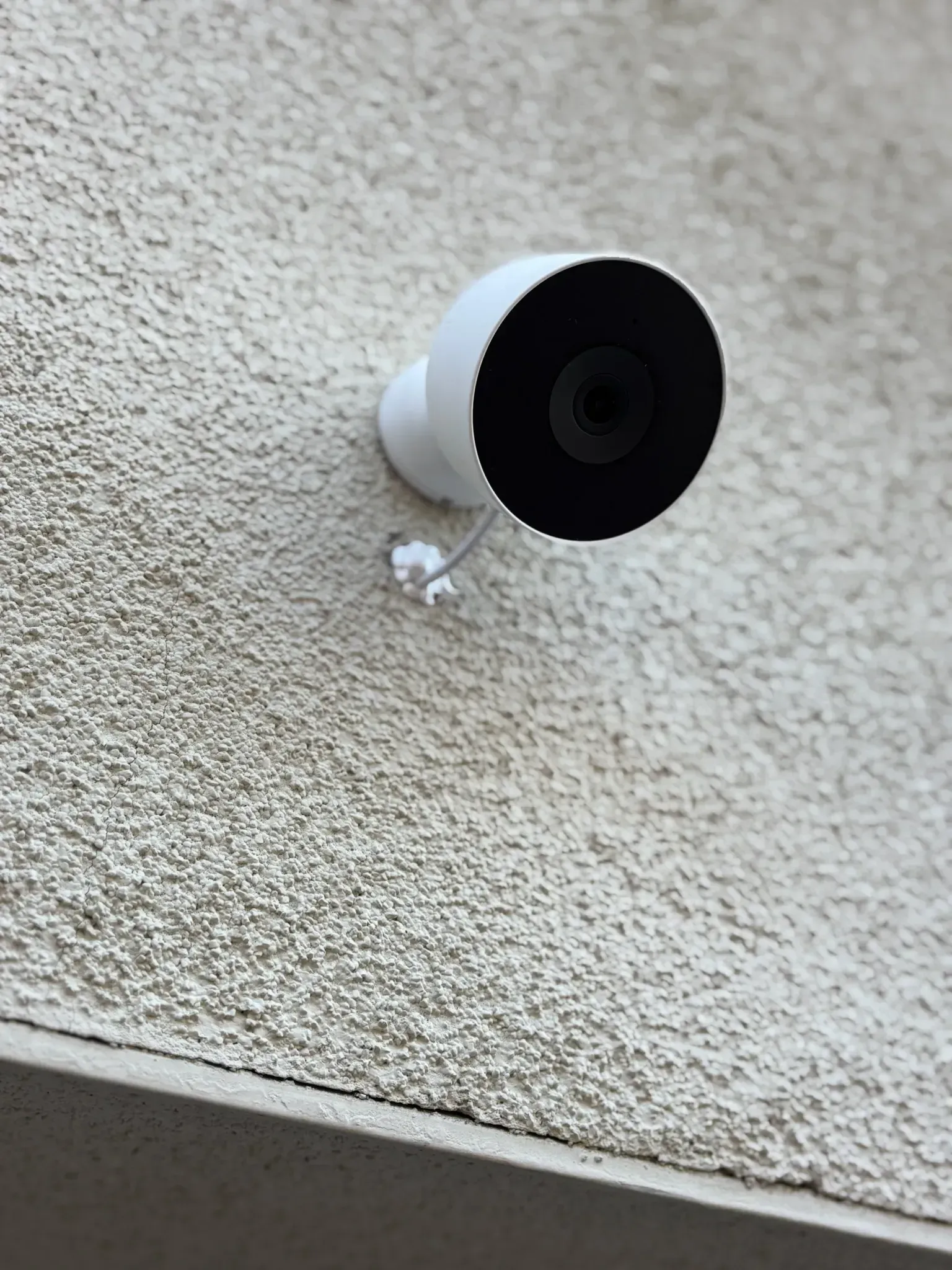 A white security camera mounted on a textured, light-colored stucco exterior wall.