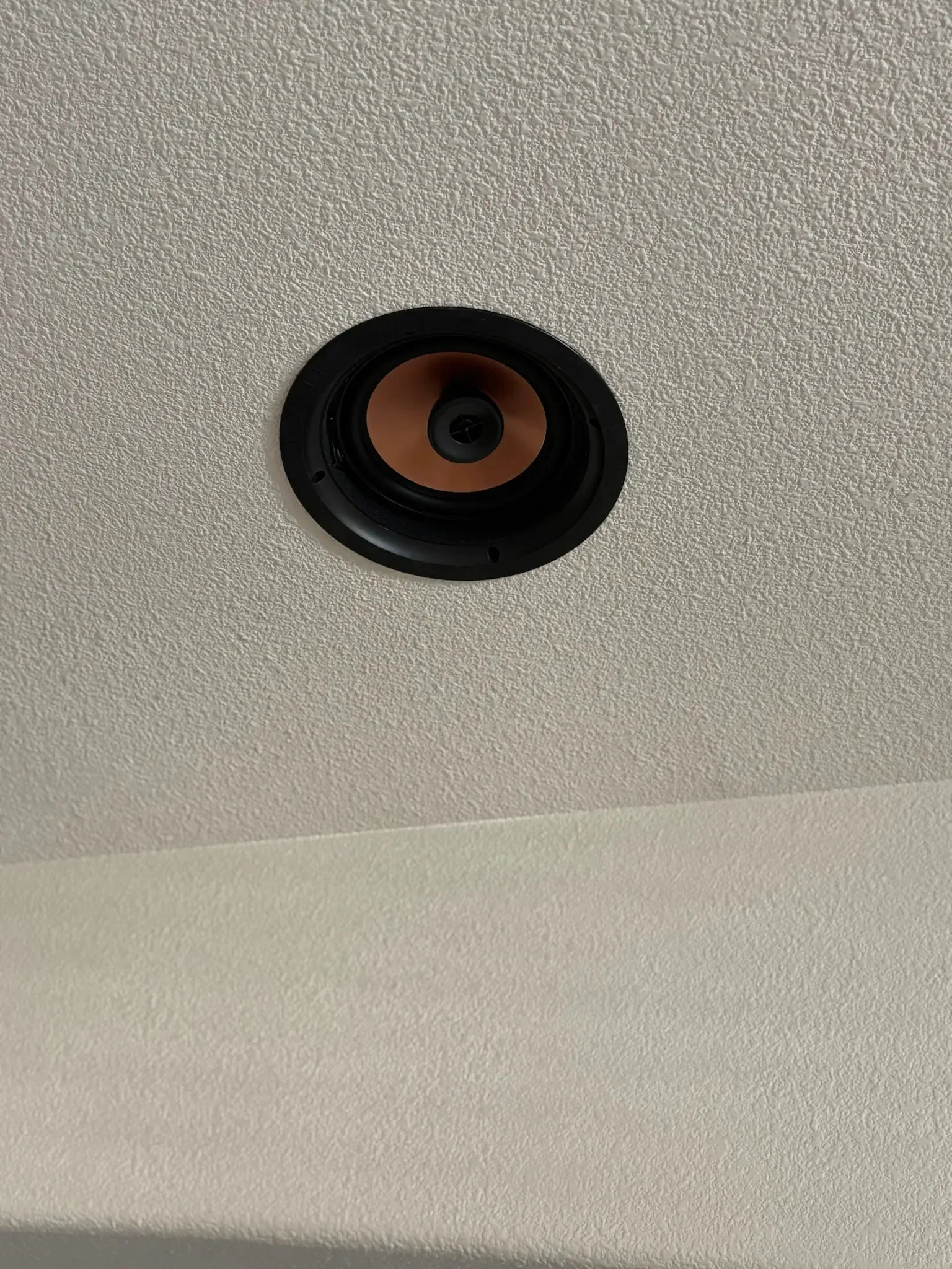 A circular speaker mounted flush in a textured, off-white ceiling.