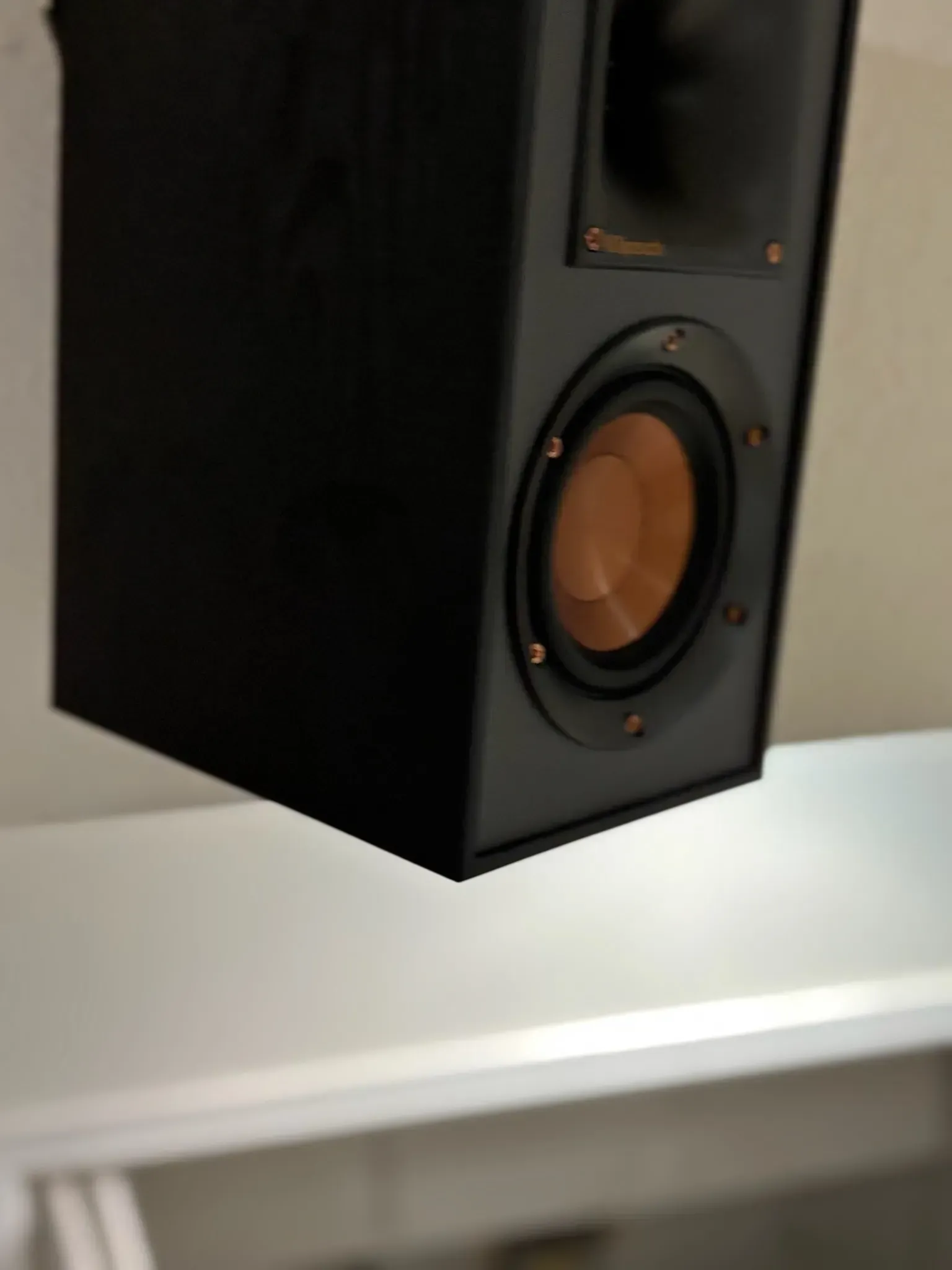 A wall-mounted black Klipsch speaker with a distinctive copper-colored woofer and a horn-loaded tweeter.